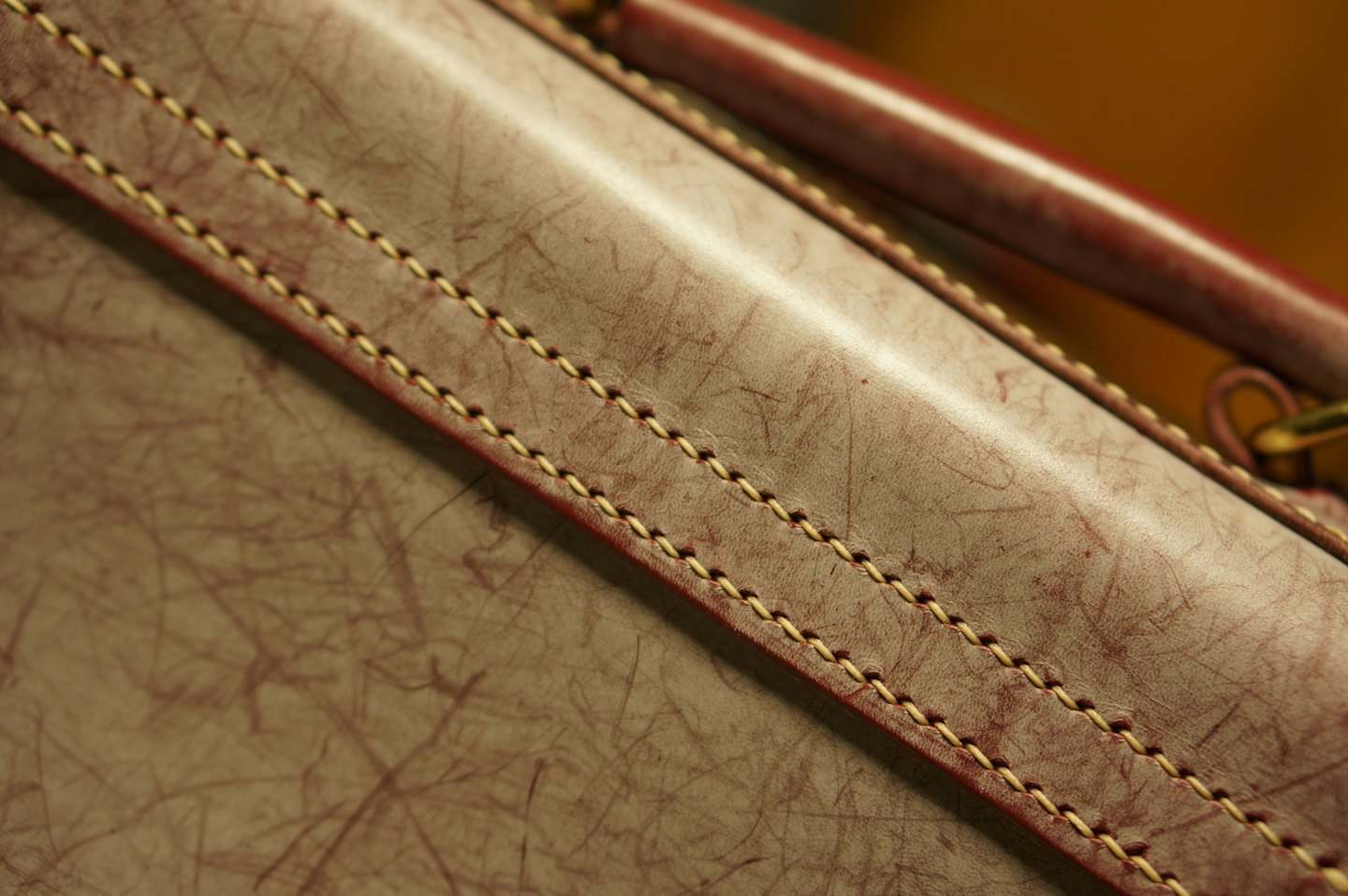 Detalles de costura en un bolso de cuero texturizado de color marrón rojizo.