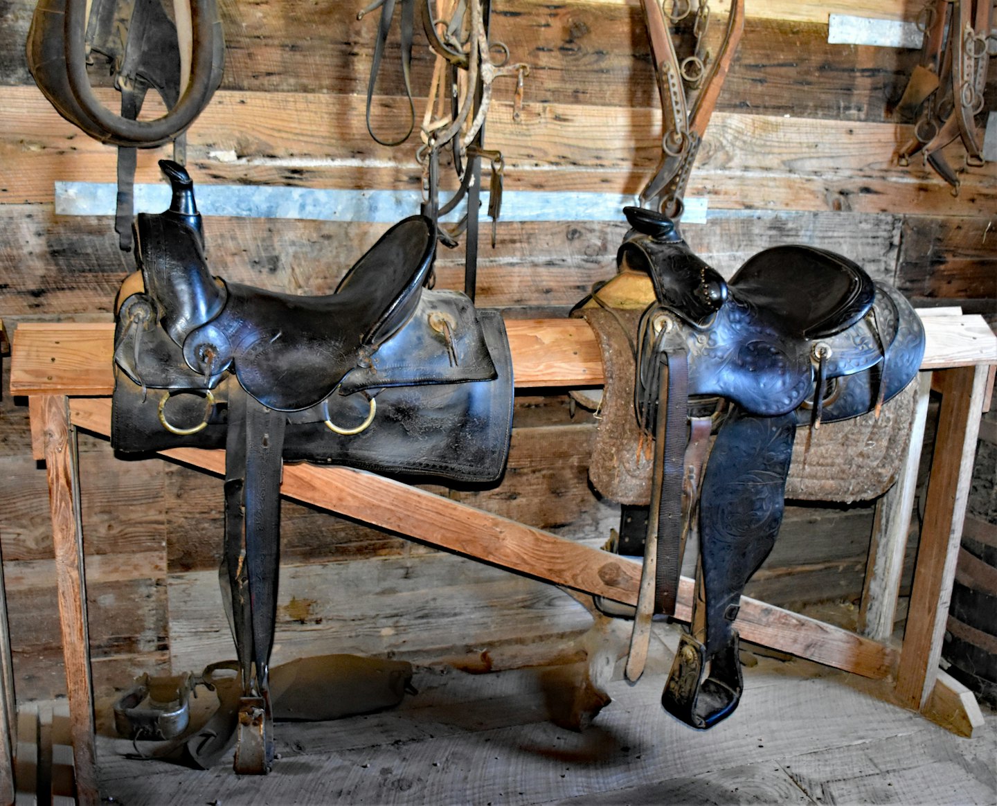 Dos sillas de montar de cuero negro para caballos sobre soportes de madera.